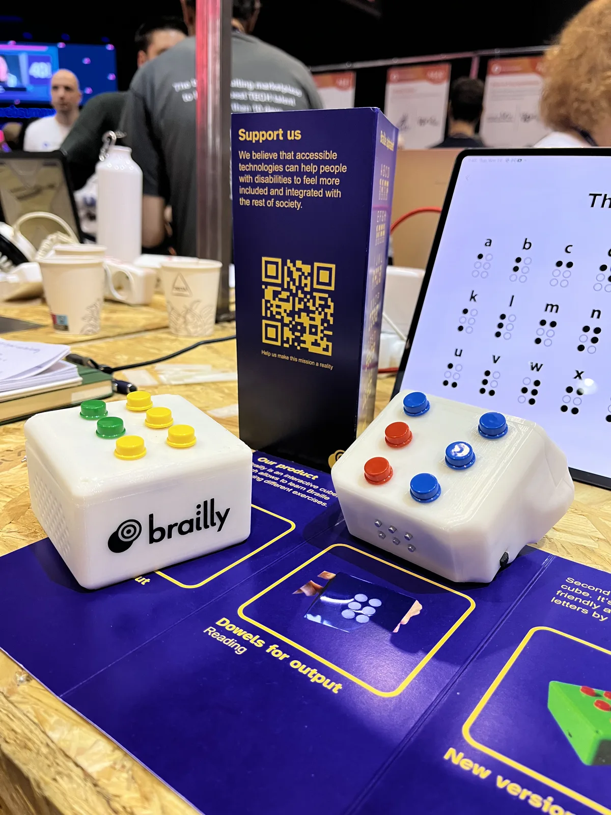 Two white Brailly prototypes with coloured buttons, a speaker, and refreshable braille pins